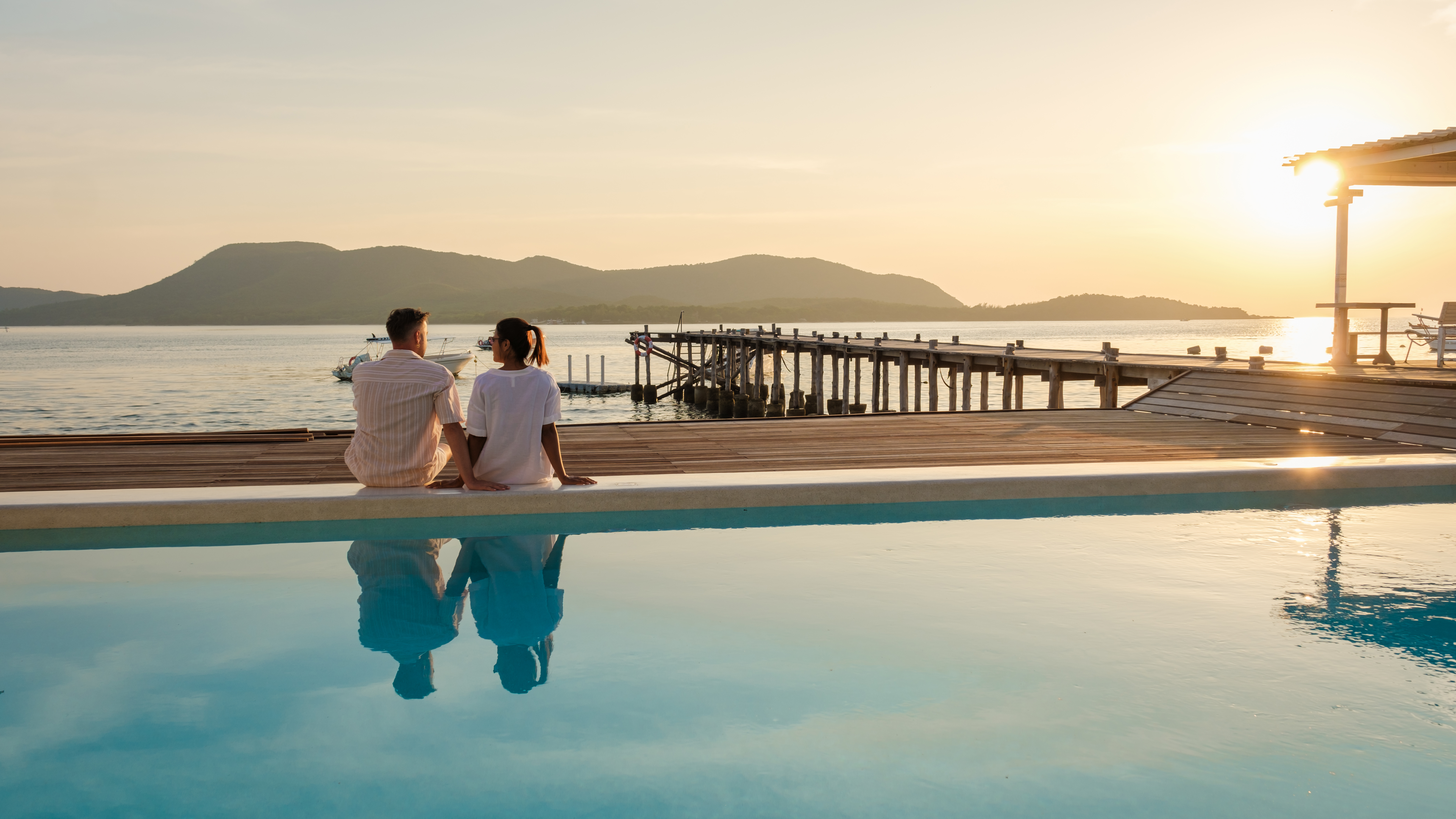 Two people looking out to sea from a hotel swimming pool.