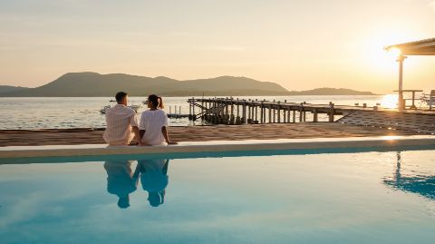 Two people looking out to sea from a hotel swimming pool.